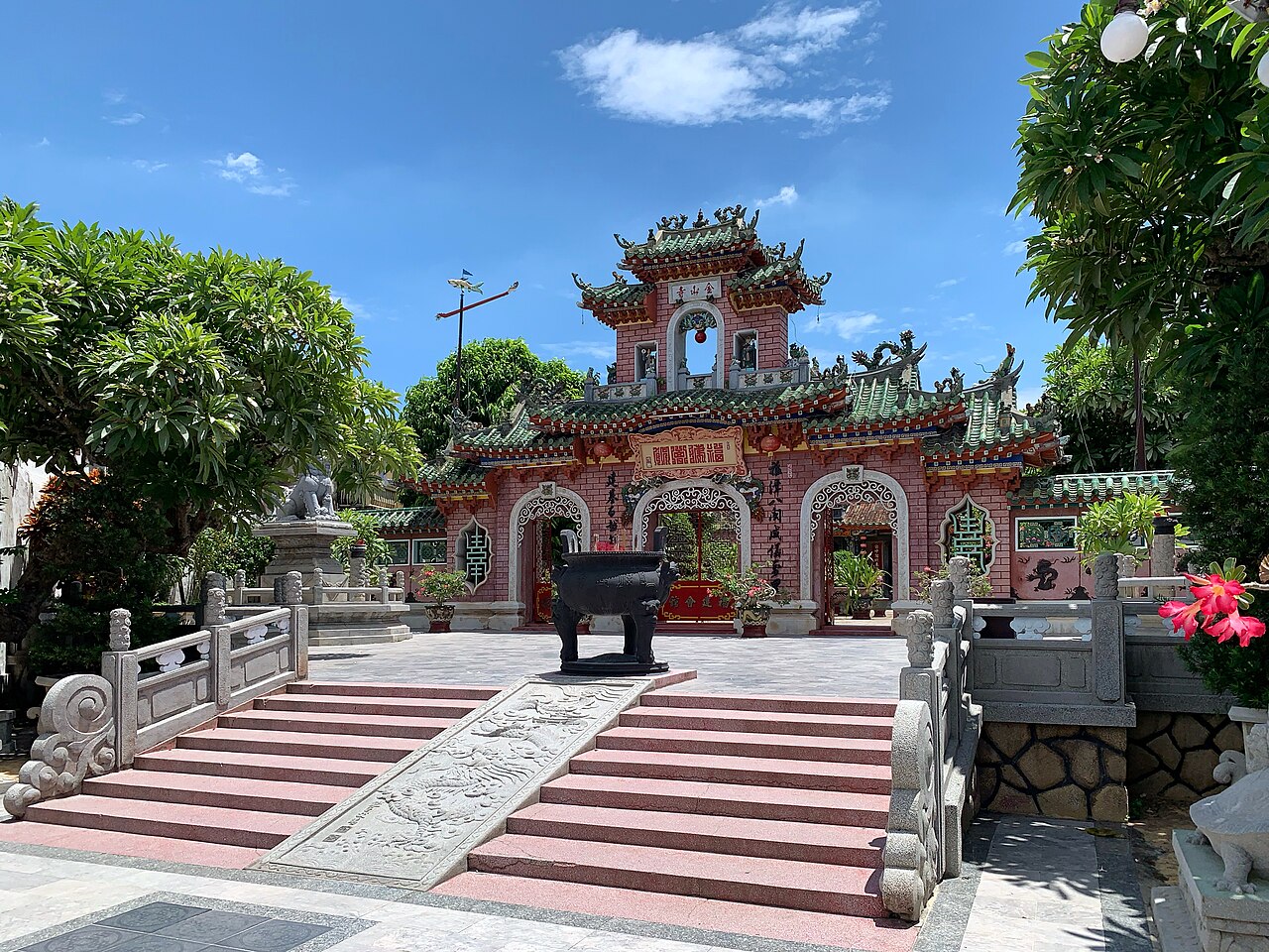 Cổng tam quan màu hồng của hội quán Phúc Kiến ở Hội An dưới trời xanh, mái lợp ngói men xanh, lư đồng đặt giữa sân và bậc thềm chạm rồng.