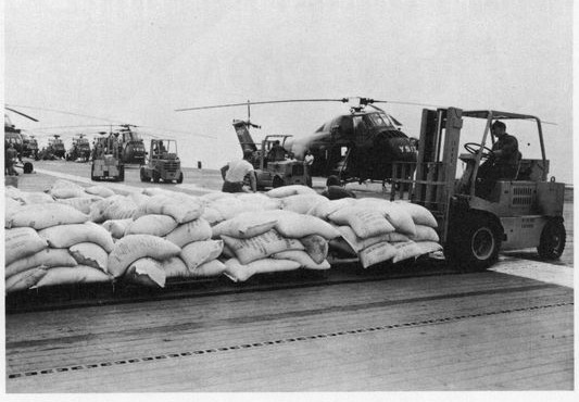 The flight deck of the USS Princeton stacked with sacks, a forklift running along the row, helicopters ranged behind.