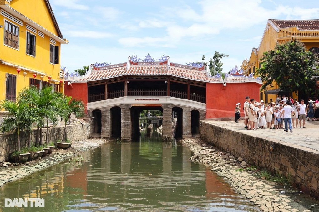 The bridge freshly repainted in bright vermilion and white, tourists gathered on the bank beside the canal.