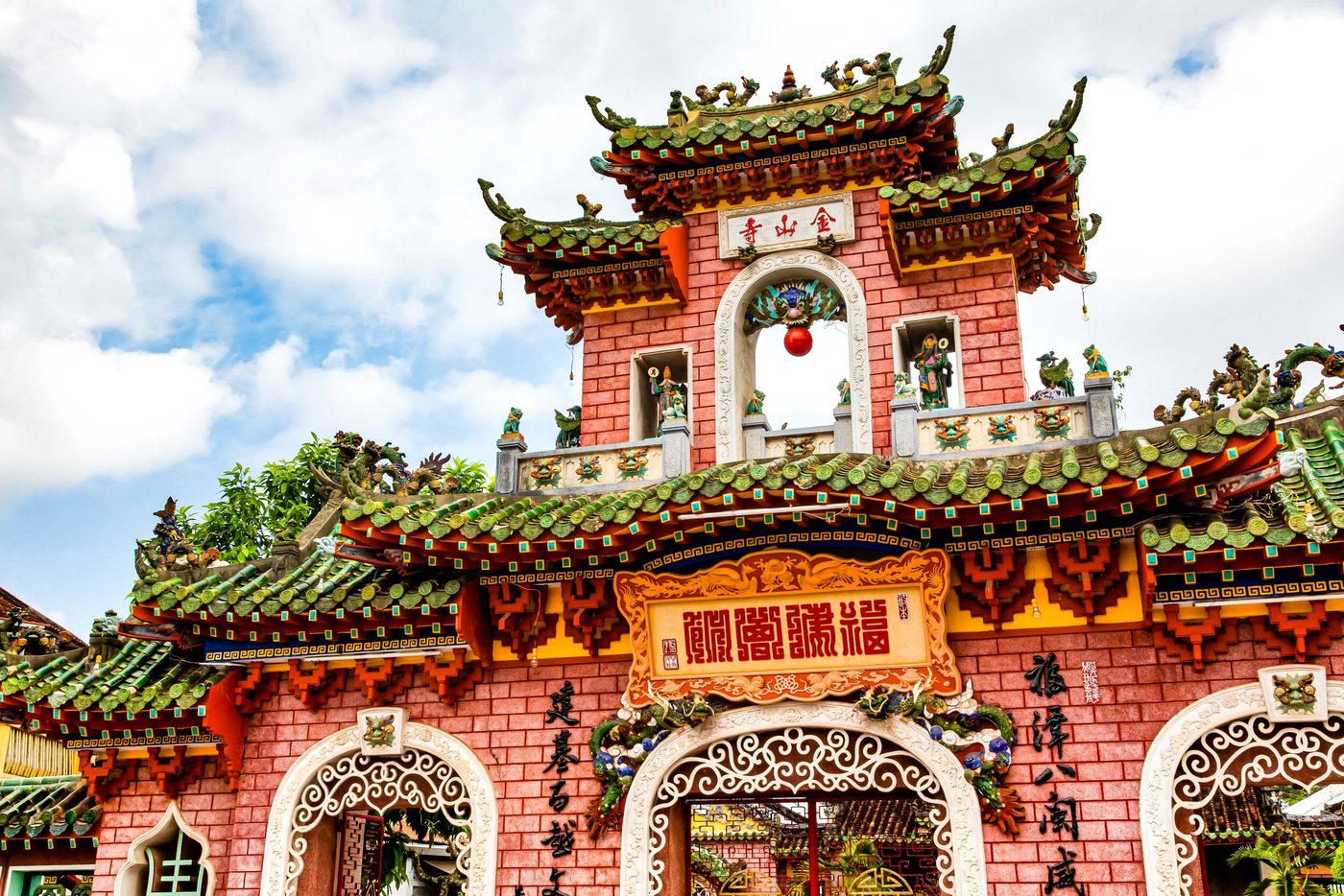 Tầng trên của cổng xây lại, bảng đá dọc khắc chữ Kim Sơn Tự đặt trong tường gạch đỏ, phía dưới mái ngói men xanh nhiều tầng, một trái cầu đỏ treo trong vòm cổng.