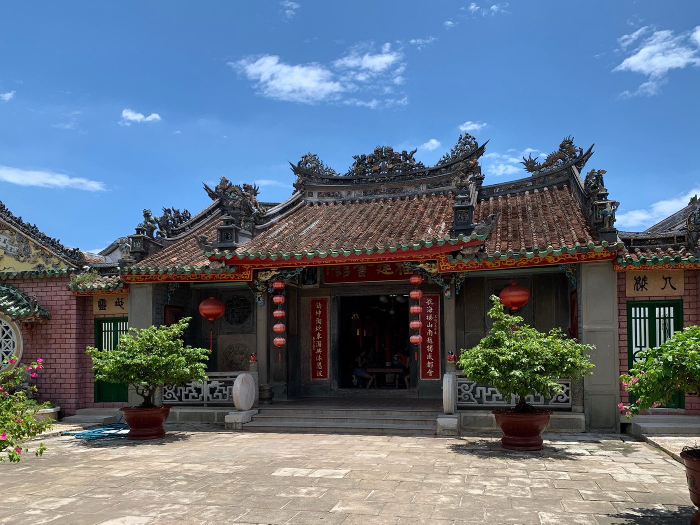 Tiền điện hội quán Phúc Kiến ở Hội An nhìn từ sân trong, mái hai tầng đắp rồng trên bờ nóc, đèn lồng đỏ và câu đối hai bên cửa chính, chậu cây cảnh phía trước.