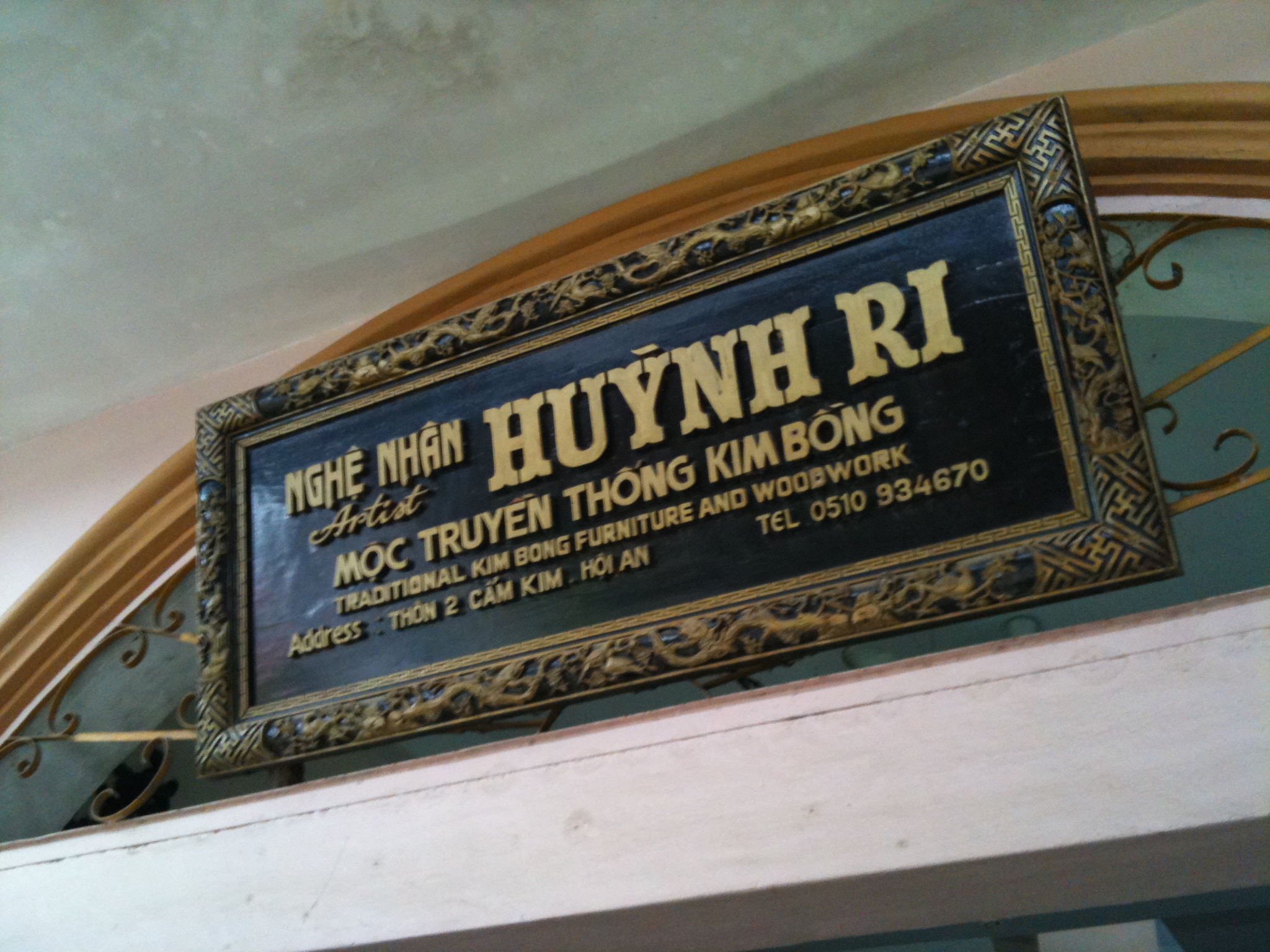 A gilt wooden sign reading NGHỆ NHÂN HUỲNH RI — MỘC TRUYỀN THỐNG KIM BỒNG — TRADITIONAL KIM BONG FURNITURE AND WOODWORK, with the workshop's address, mounted above an archway.