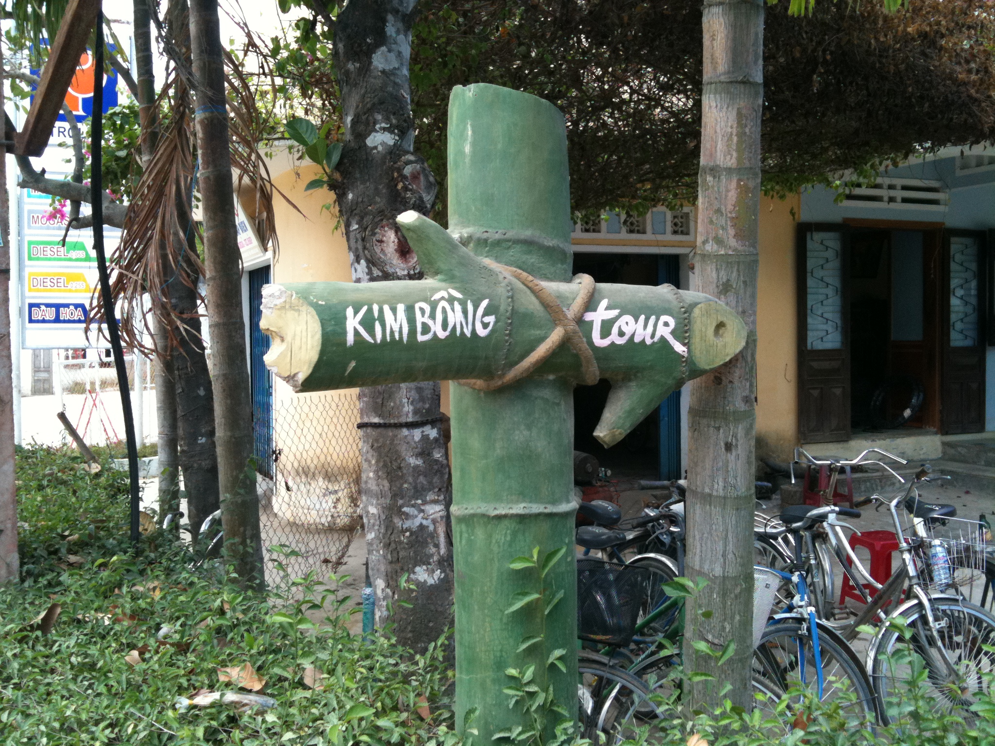 A hand-painted bamboo signpost pointing the way with the words KIM BONG tour, bicycles parked against a wall behind it.