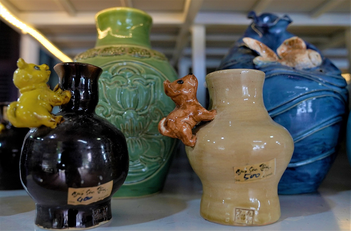 Four small glazed vases in black, green, pale yellow and blue, each with a small animal figure climbing its shoulder, price tags attached to the pieces.