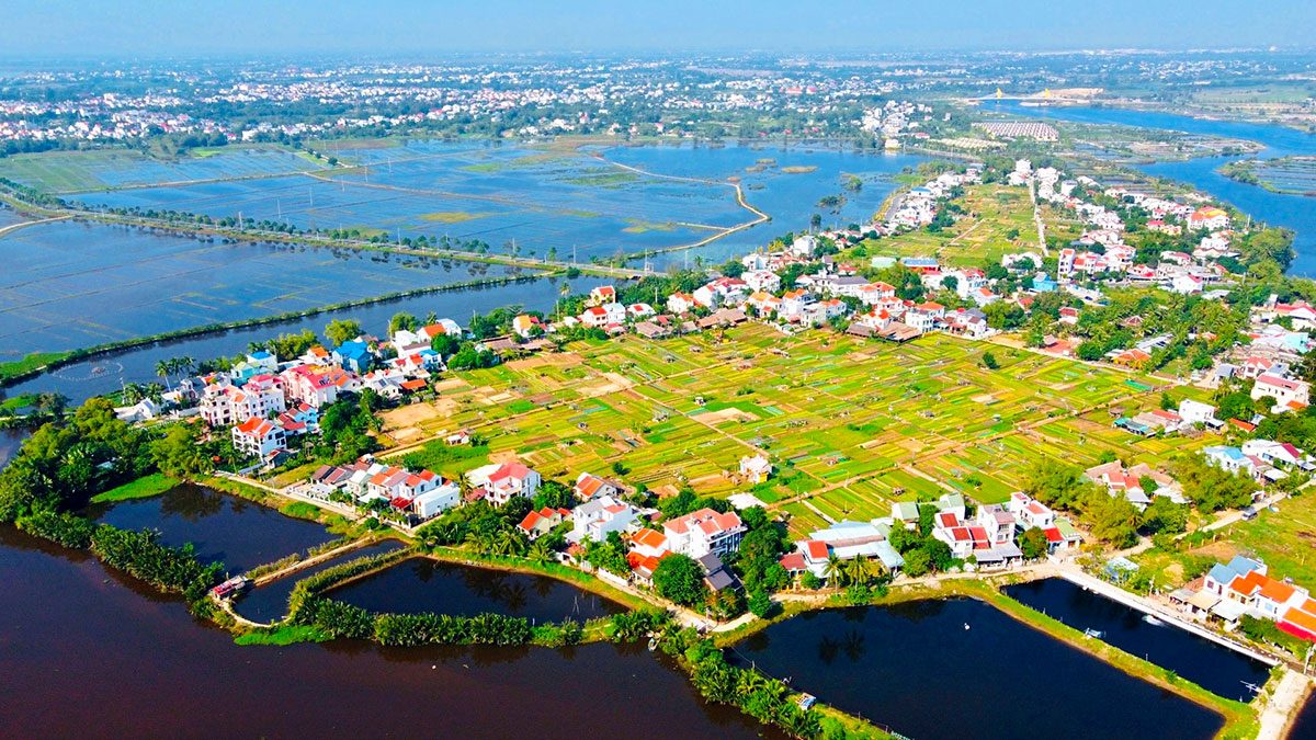 The vegetable village seen from above: a patch of yellow and green ground with houses lies among dark blue-green water, with water on two sides.
